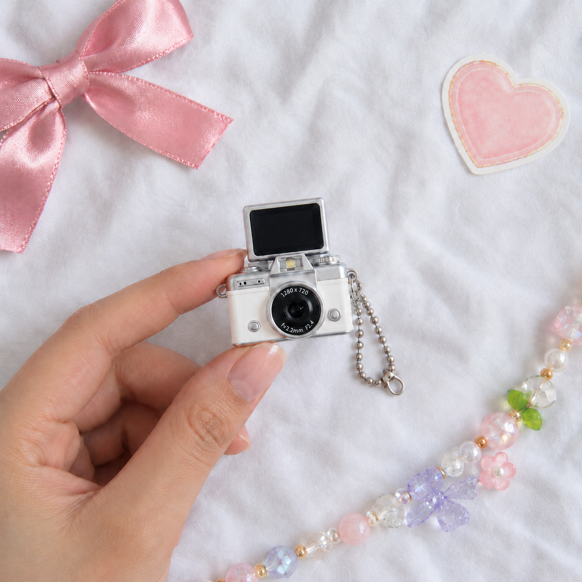 Mini Flip Screen Keychain Camera in White, held between thumb and finger for size