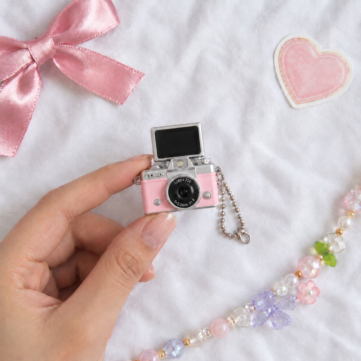 Mini Flip Screen Keychain Camera in Pink, held between thumb and finger for size