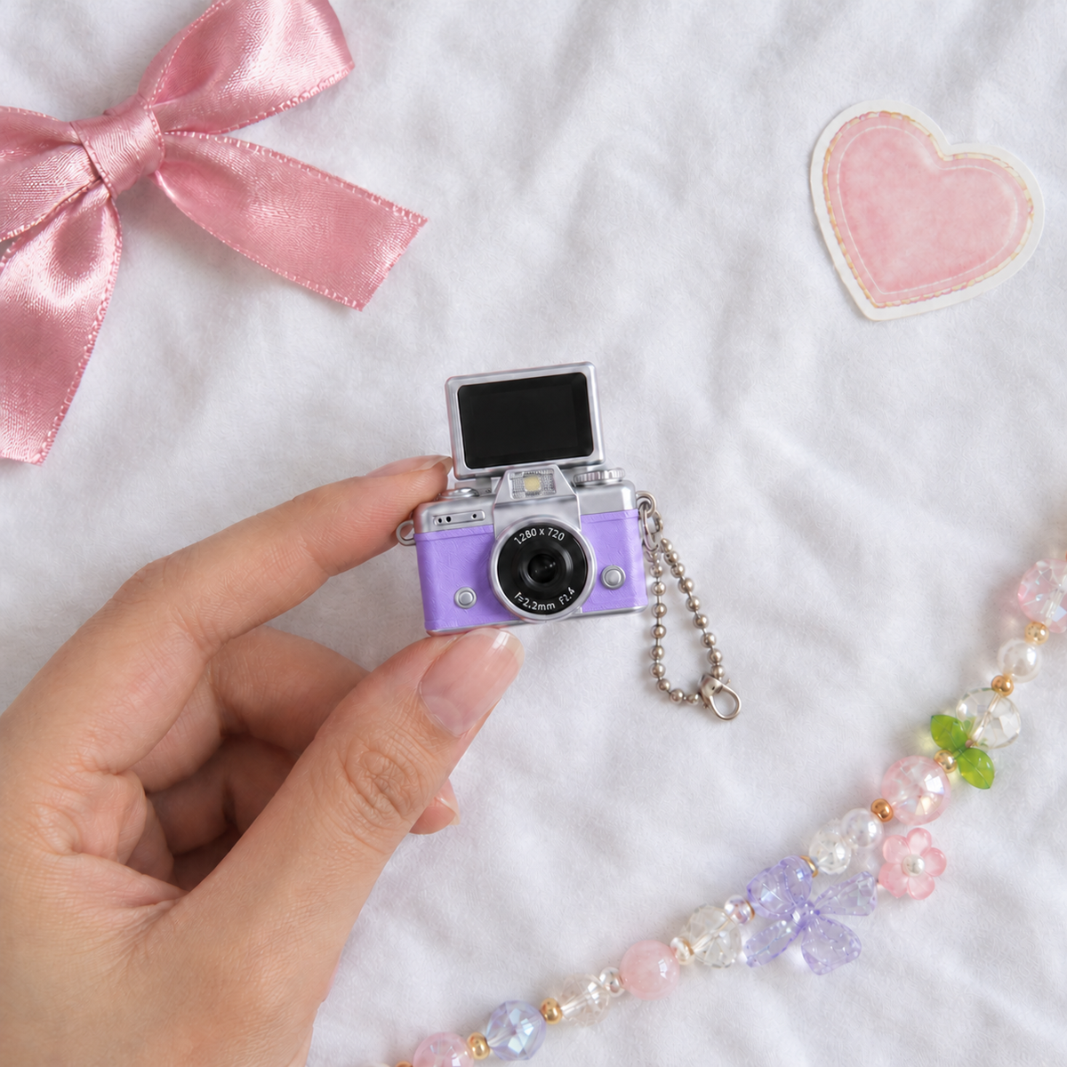 Mini Flip Screen Keychain Camera in Purple, held between thumb and finger for size